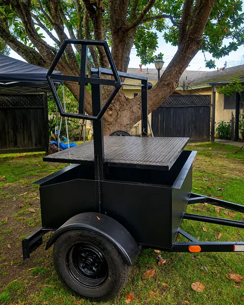 The Oak & Ember Santa Maria grill trailer under an oak tree, with the hexagonal crank wheel above the grate